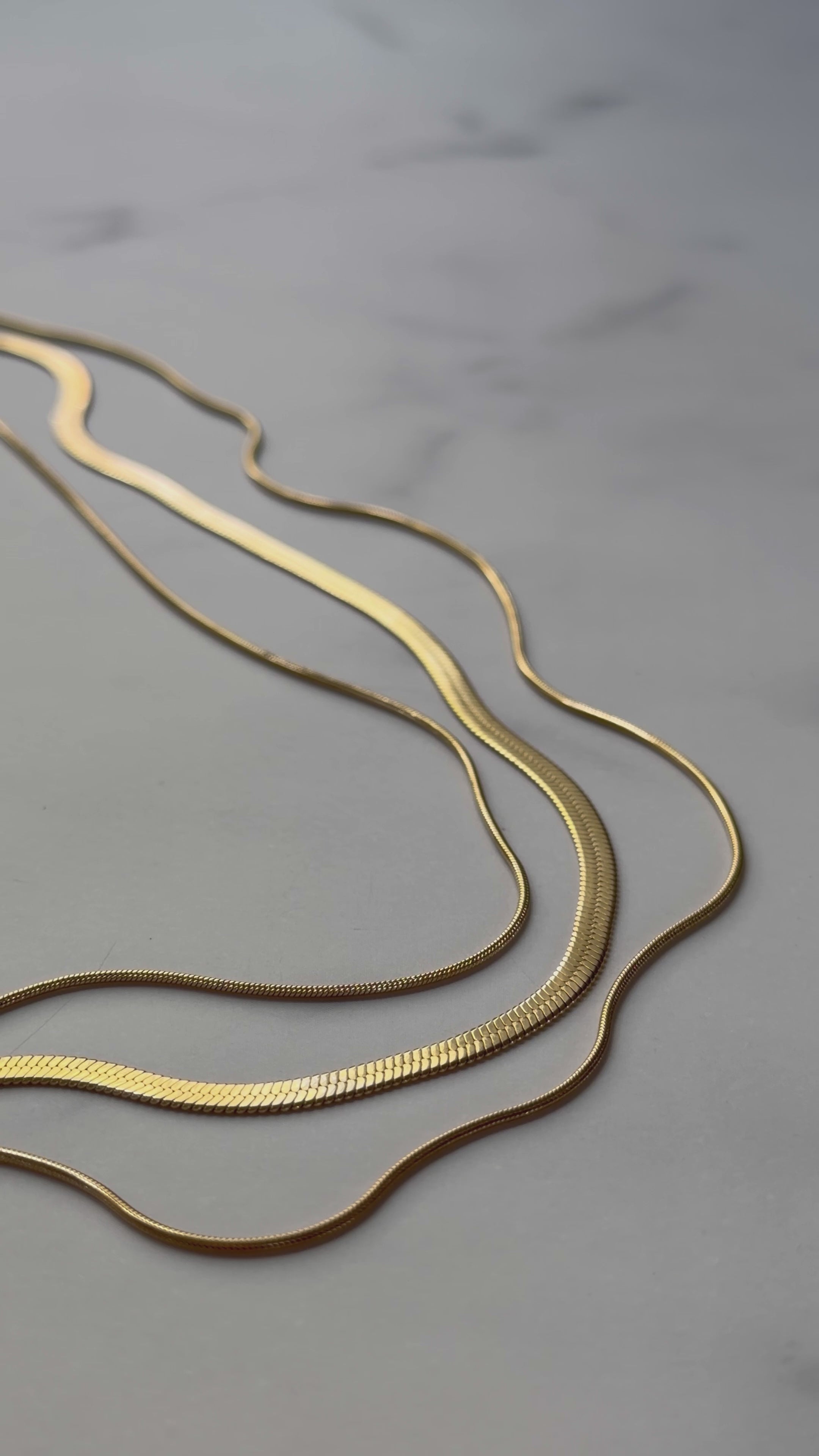 RALLUNA triple chain gold necklace displayed on a marble surface