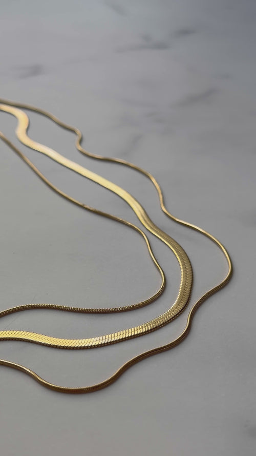 RALLUNA triple chain gold necklace displayed on a marble surface