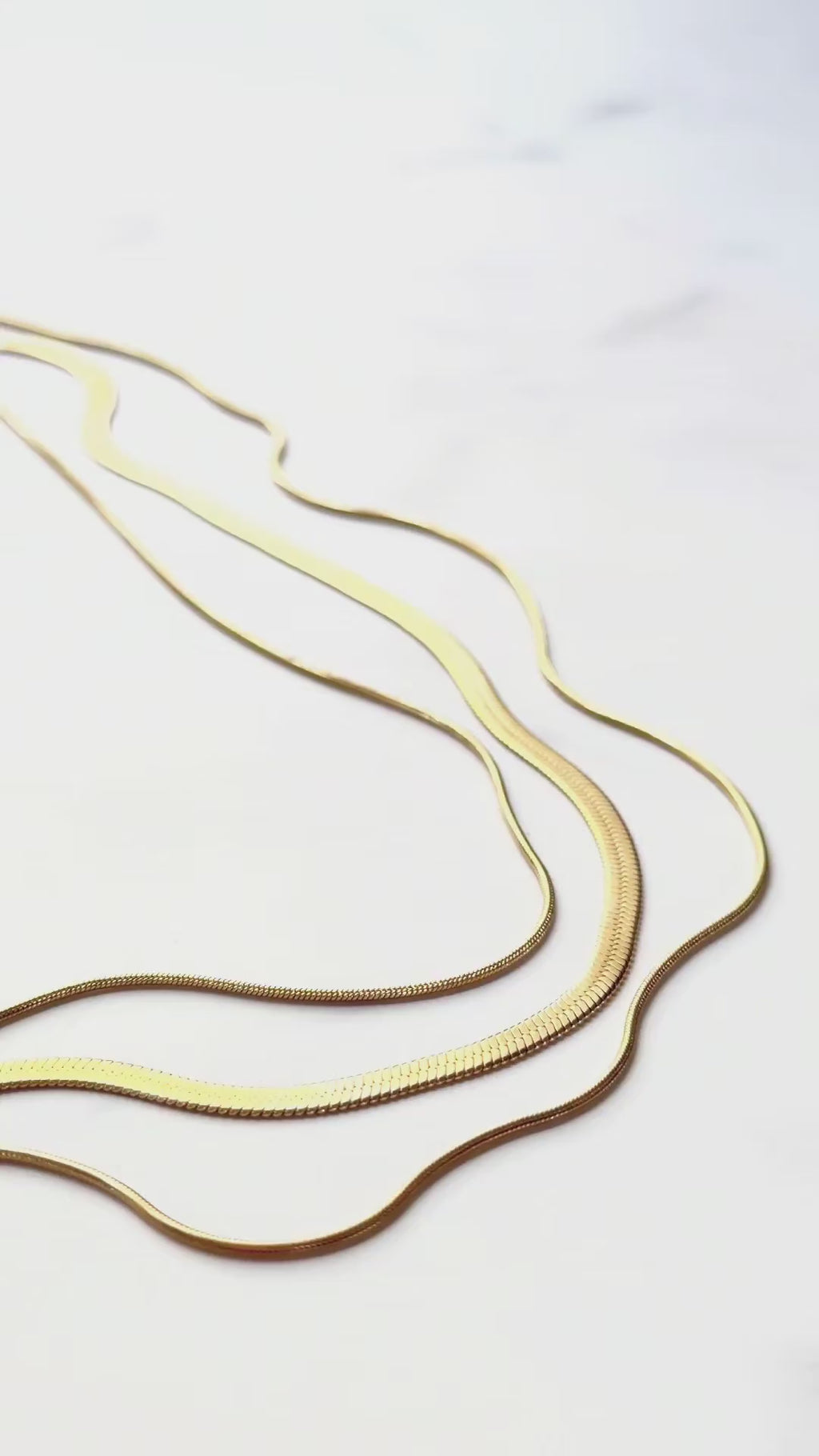 Close-up video of the RALLUNA Triple Layer Herringbone Necklace in gold-tone 316 stainless steel showing its texture and fluid movement on a white background