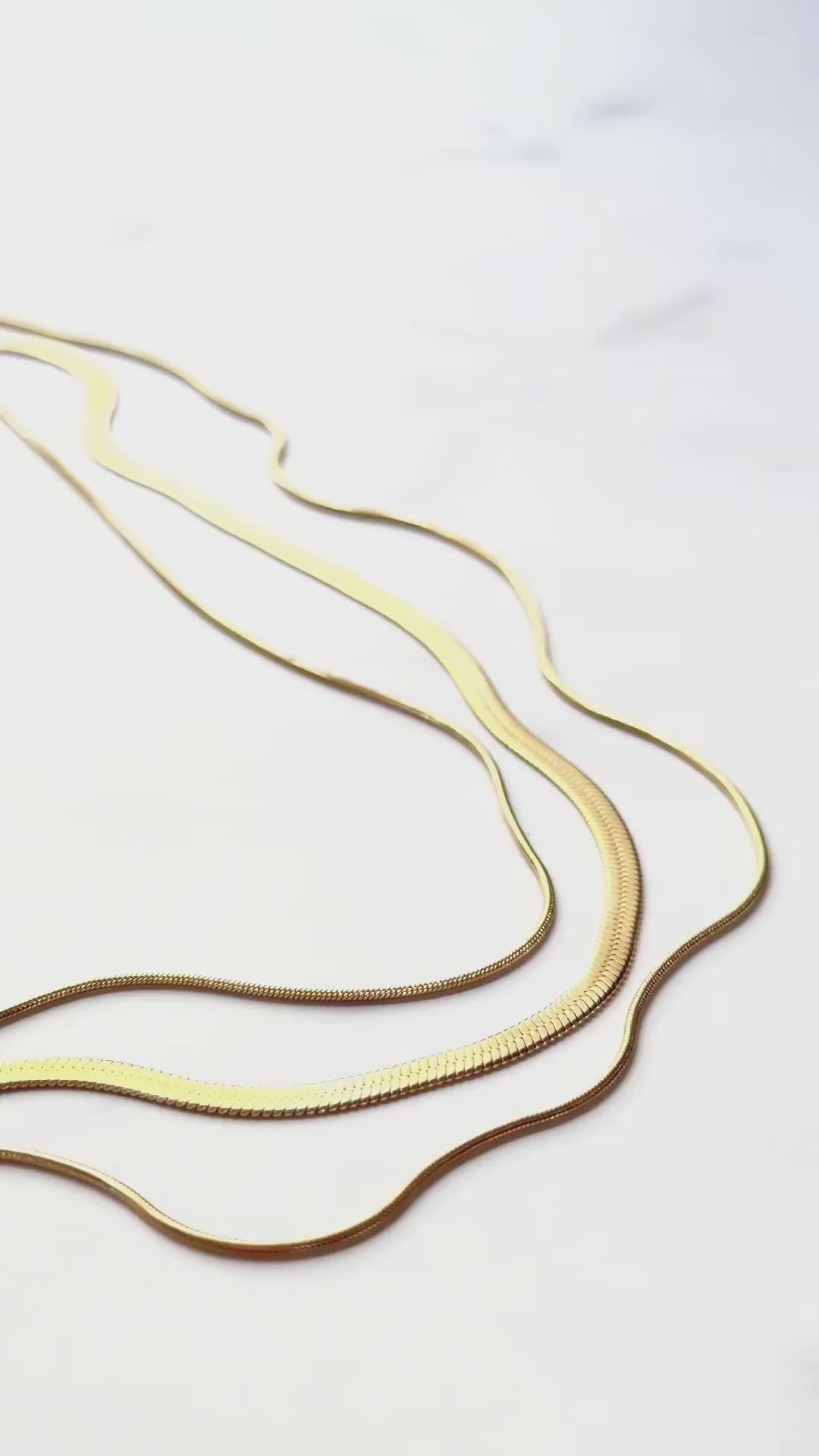 Close-up video of the RALLUNA Triple Layer Herringbone Necklace in gold-tone 316 stainless steel showing its texture and fluid movement on a white background